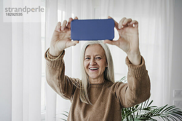 Glückliche reife Frau  die zu Hause mit dem Smartphone fotografiert