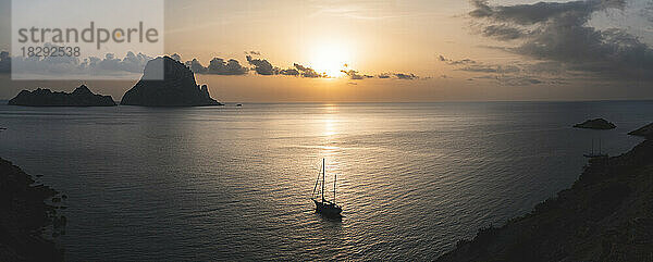 Spanien  Balearen  Segelboot schwimmt bei Sonnenuntergang in Küstennähe mit der Insel Es Vedra im Hintergrund