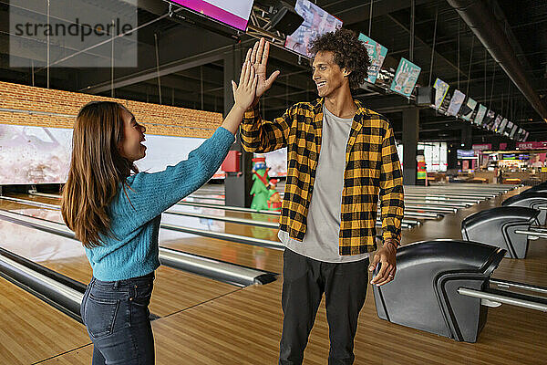 Young woman giving high five to friend at bowling alley