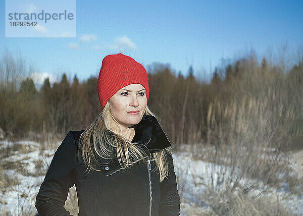 Nachdenkliche Frau mit roter Strickmütze blickt auf die Winterlandschaft