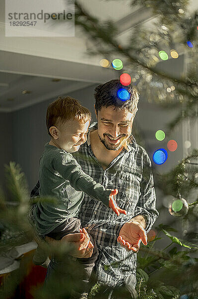 Glücklicher Vater und Sohn stehen zu Hause vor dem Weihnachtsbaum
