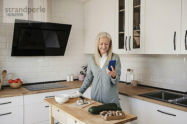 Glückliche reife Frau benutzt Smartphone in der Küche