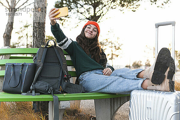Fröhliches Mädchen  das auf einer Bank sitzt und ein Selfie mit dem Smartphone macht