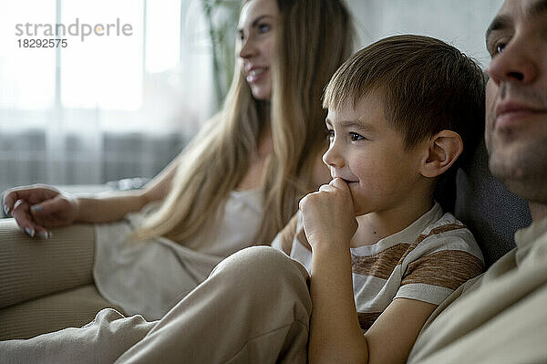 Lächelnder Sohn verbringt seine Freizeit mit den Eltern zu Hause auf dem Sofa