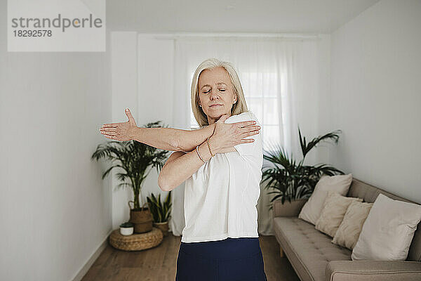 Frau streckt Arm aus und trainiert im Wohnzimmer