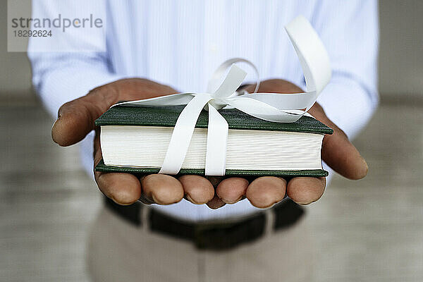 Hände eines Mannes  der ein mit weißem Band gebundenes Buch hält