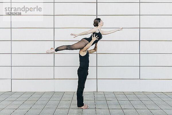 Mann hebt Frau  die vor der Wand Balletttanz übt