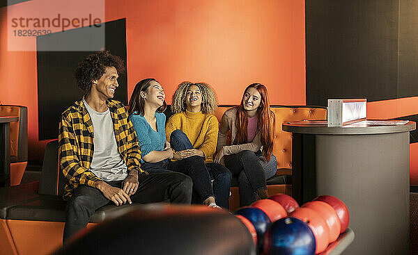 Fröhliche gemischtrassige Freunde sitzen auf dem Sofa und genießen die Bowlingbahn