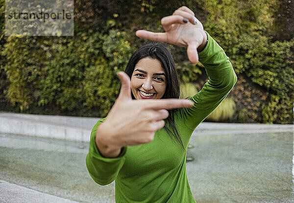 Lächelnde Frau macht mit den Fingern einen Rahmen vor einem vertikalen Garten