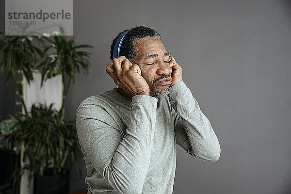 Mature man enjoying music listening through wireless headphones in front of gray wall