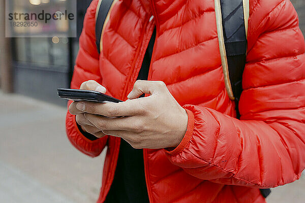 Hände eines jungen Mannes  der sein Mobiltelefon benutzt