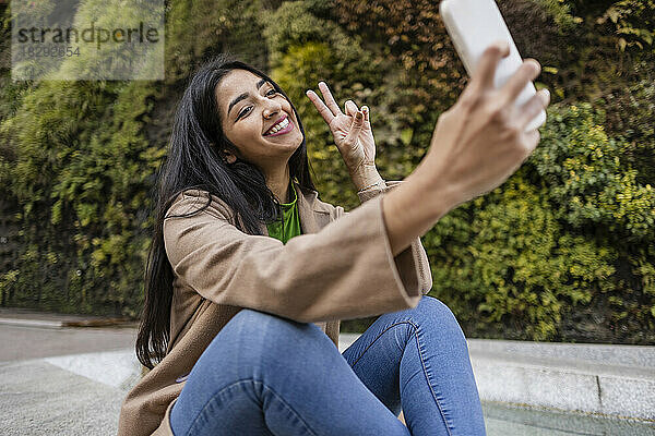Glückliche junge Frau  die draußen im vertikalen Garten ein Selfie mit ihrem Smartphone macht