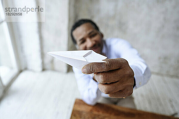 Reifer Geschäftsmann spielt im Büro mit Papierflieger