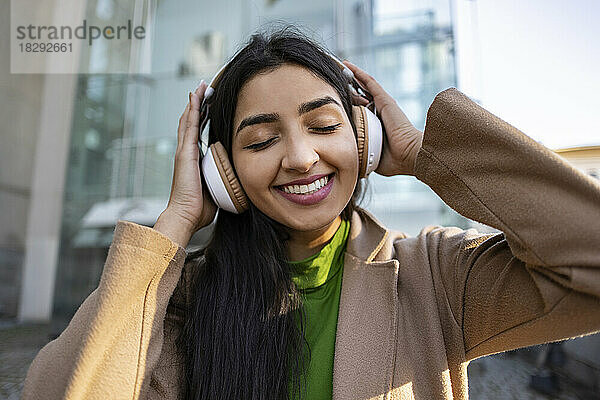Glückliche Frau mit Kopfhörern  die vor dem Gebäude Musik hört