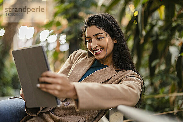 Glückliche junge Frau sitzt am Geländer und benutzt einen Tablet-Computer