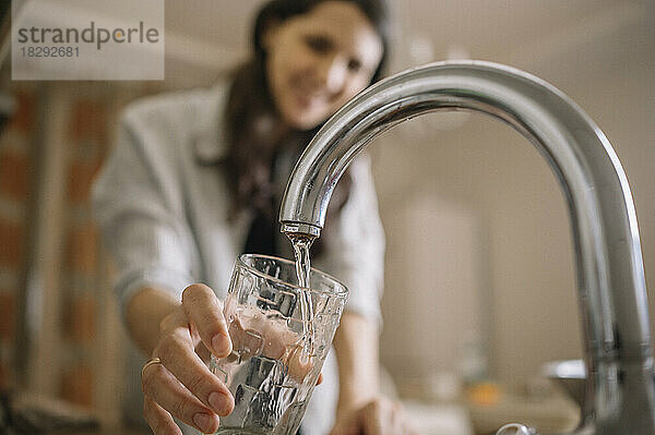 Woman filling water from faucet in glass at home
