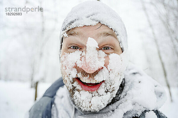 Glücklicher Mann mit schneebedecktem Gesicht im Winterpark