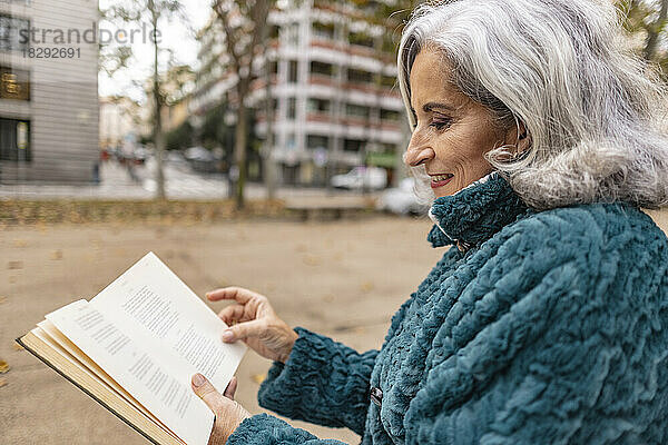 Lächelnde ältere Frau liest Buch am Fußweg