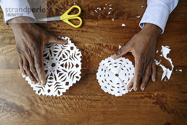 Hands of man holding paper snowflakes on table