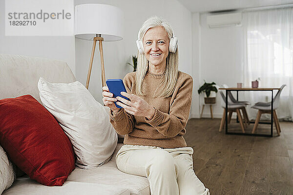 Glückliche reife Frau mit Smartphone sitzt auf dem Sofa