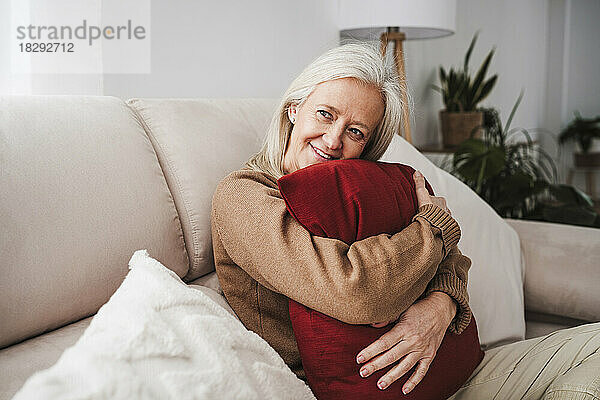 Thoughtful mature woman hugging cushion in living room