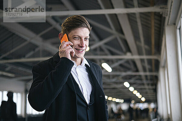 Glücklicher Geschäftsmann  der am Bahnhof über sein Mobiltelefon spricht