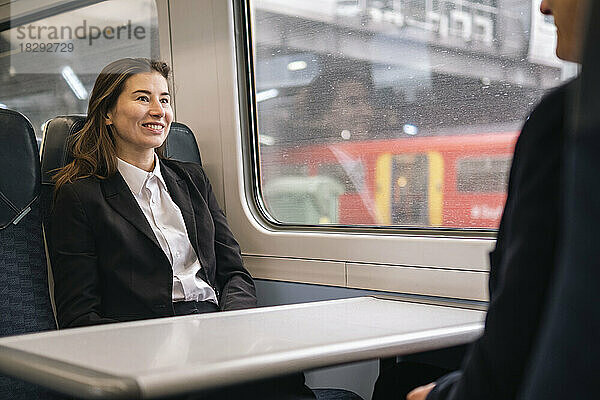 Glückliche Geschäftsfrau mit Kollegin  die im Zug am Fenster sitzt