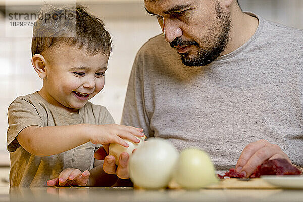 Glücklicher Junge  der zu Hause in der Küche weiße Zwiebeln vom Vater nimmt