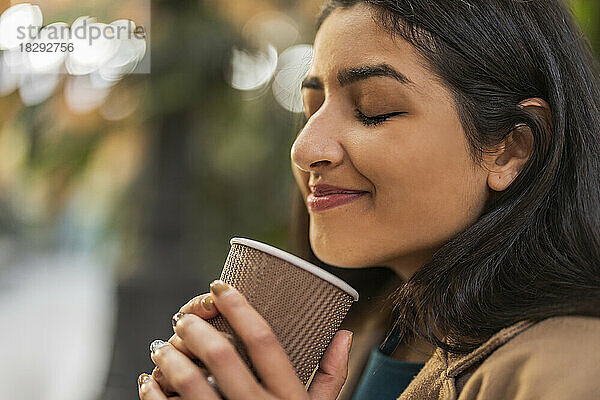 Lächelnde Frau mit geschlossenen Augen hält eine Einweg-Kaffeetasse in der Hand
