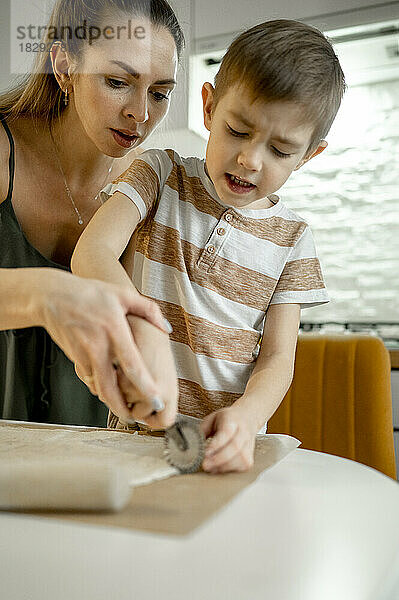 Mutter und Sohn schneiden Croissant-Teig auf dem Tisch in der heimischen Küche