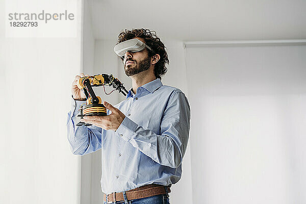 Geschäftsmann mit VR-Brille hält Roboterarm im Büro
