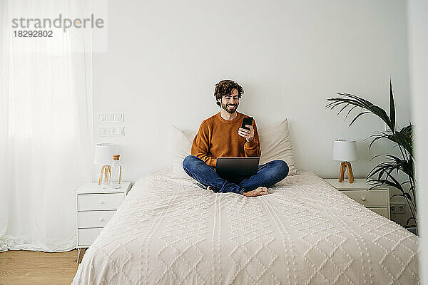 Glücklicher Freiberufler  der sein Smartphone zu Hause im Bett nutzt