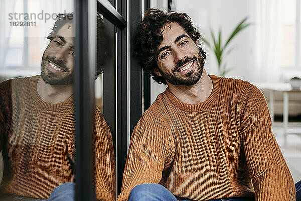 Happy young man leaning on glass door at home