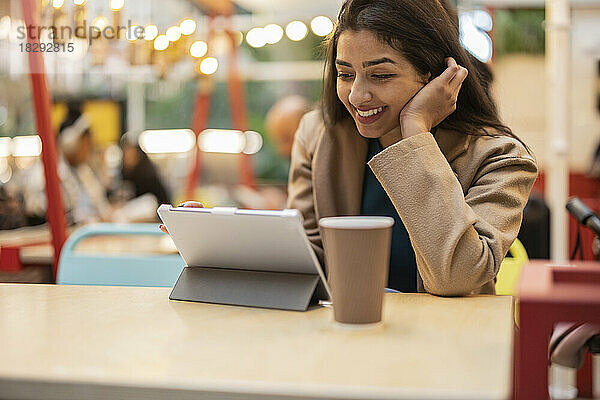 Glückliche junge Frau benutzt Tablet-Computer im Café