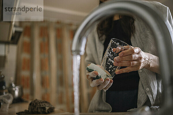 Frau wäscht Trinkglas vor fließendem Wasser aus dem Wasserhahn zu Hause