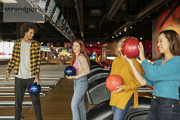 Happy multiracial friends holding ball enjoying at bowling alley