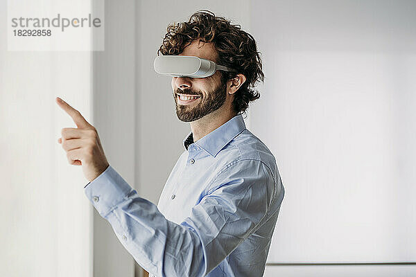 Glücklicher Geschäftsmann mit Virtual-Reality-Brille gestikuliert im Büro