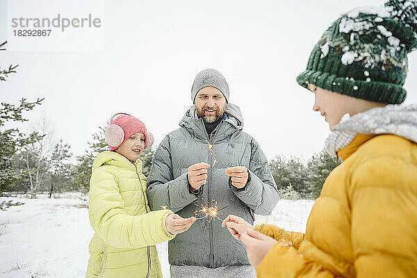 Lächelnder Mann mit Sohn und Tochter  die Feuer halten  funkelt im Schnee