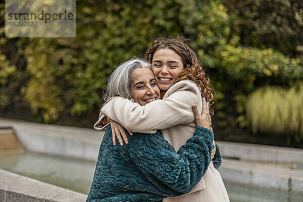 Glückliche junge Frau umarmt Großmutter im Park