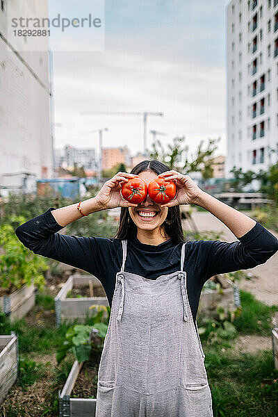 Glückliche junge Frau hält im Stadtgarten Tomaten über die Augen