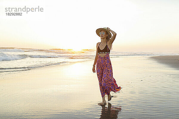 Junge Frau mit Hut spaziert am Strand entlang