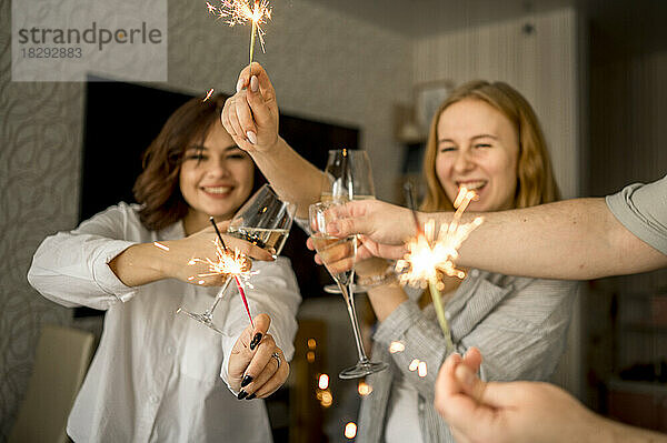 Fröhliche Freunde feiern zu Hause mit Gläsern Champagner und Wunderkerzen