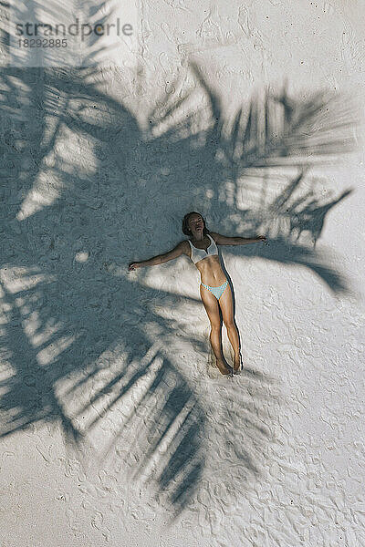 Luftaufnahme einer Frau  die im Schatten eines Baumes auf Sand liegt