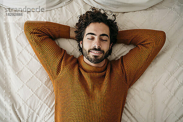 Smiling man with eyes closed lying on bed at home