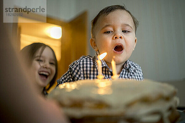 Junge bläst Kerzen auf Kuchen und feiert zu Hause seinen Geburtstag