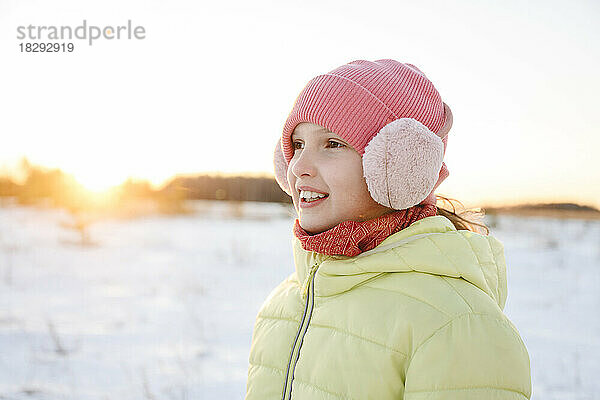 Fröhliches Mädchen mit Strickmütze und Ohrenschützer im Winterwald