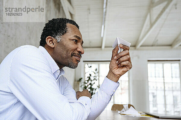 Smiling businessman looking at paper airplane in office