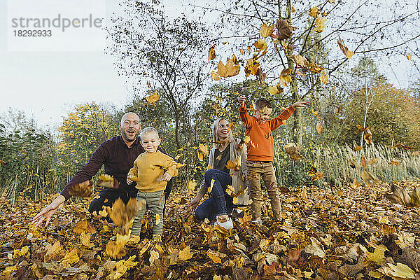 Glückliche Eltern mit verspielten Kindern  die Herbstblätter in den Wald werfen