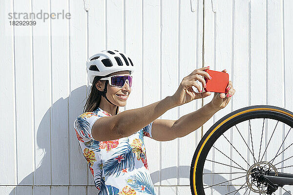 Glücklicher Radfahrer  der vor der Wand ein Selfie mit dem Smartphone macht