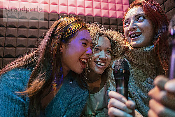 Glückliche junge Frauen singen Karaoke im Mikrofon in der Spielhalle